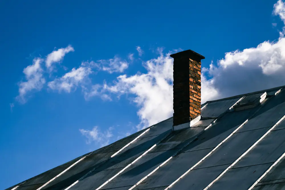 Standing-seam metal roof and brick chimney against blue sky