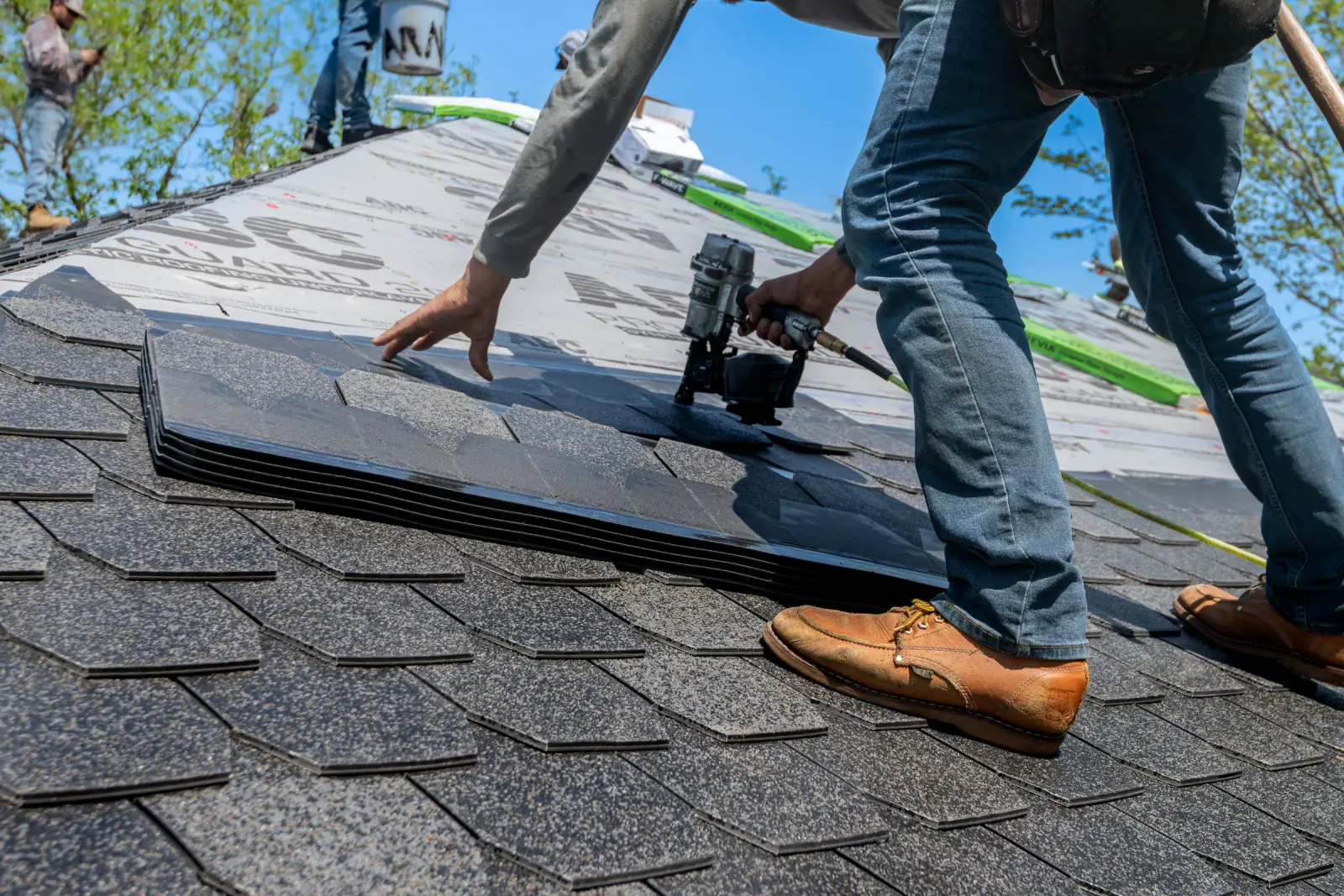 Roofer using a nail gun to fasten asphalt shingles